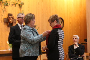 Kirsi Urkko kiinnittää Leila Hertzbergin rintaan seurakuntatyön kultaisen ansiomerkin.