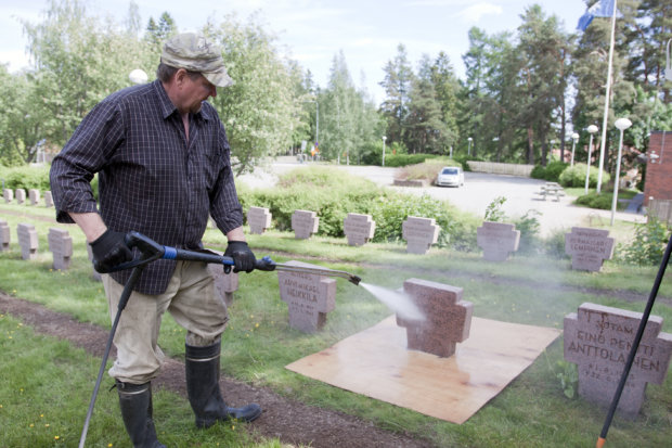 Hannu Liesilä pesi sankarihautausmaan kiviä kuumapainepesurilla. Nurmen suojaksi reserviläiset ovat nikkaroineet puulevyt.