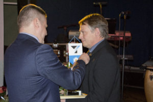 Pirkanmaan Yrittäjien varapuheenjohtaja Jari Haapaniemi kiinnittää pinssiä Pälkäneen Vuoden Yrittäjä -palkinnon saaneelle Simo Laaksolle.